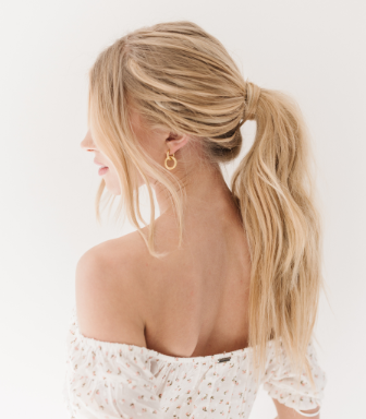 Blonde model wearing long hair extensions styled in a messy ponytail looking towards the left with a floral spring shirt